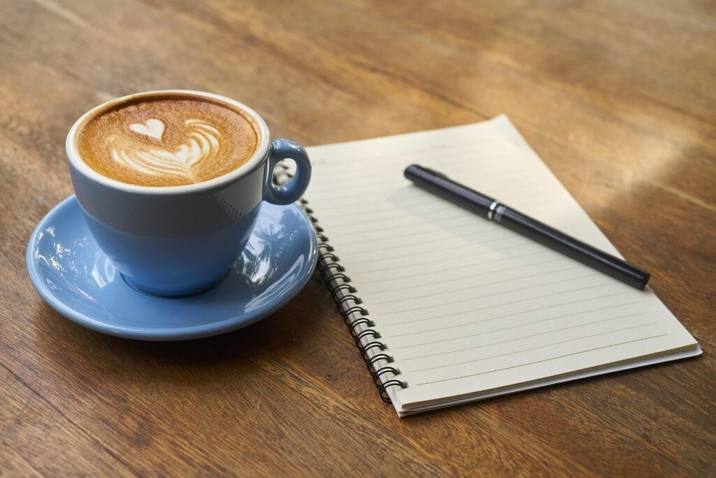 Open notebook and pen beside a cup of coffee